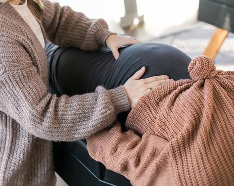 Chiropractor A chiropractor assists a baby lying on a pillow while a young boy watches, smiling.